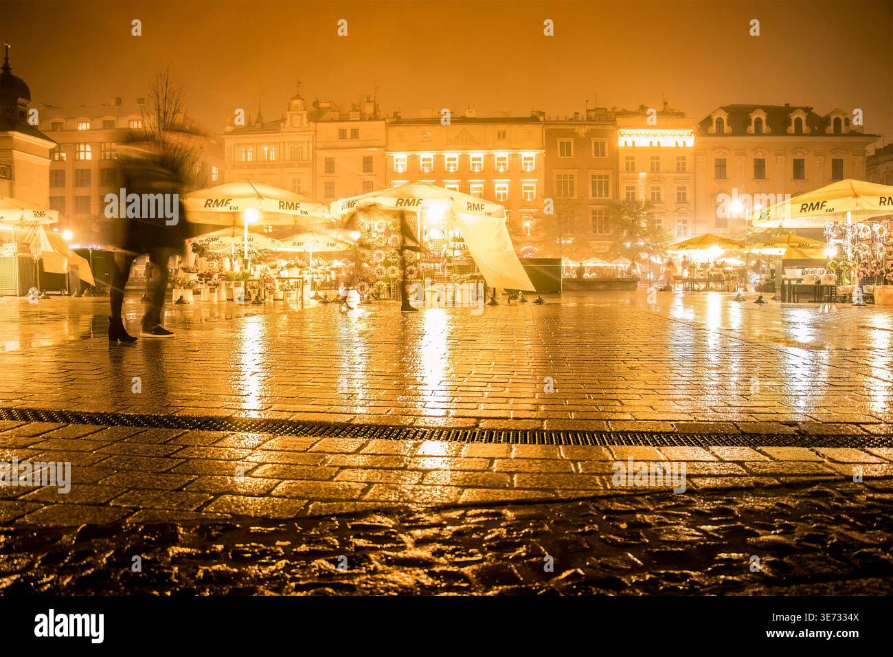 Vista notturna della piazza principale del mercato a Cracovia in Polonia durante la nebbia con ciottoli bagnati e bancarelle illuminate con ombrelli con logo RMF FM Foto Stock