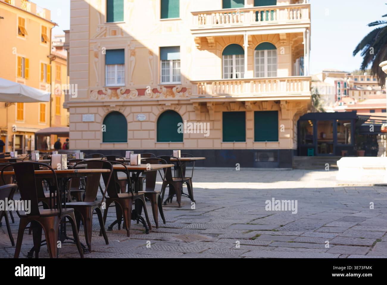 Terrazza vuota del ristorante con tavoli e sedie nella soleggiata piazza mediterranea con spazio per fotocopie. Lo scatto ad angolo basso è caratterizzato dalla tradizionale architettura italiana Foto Stock