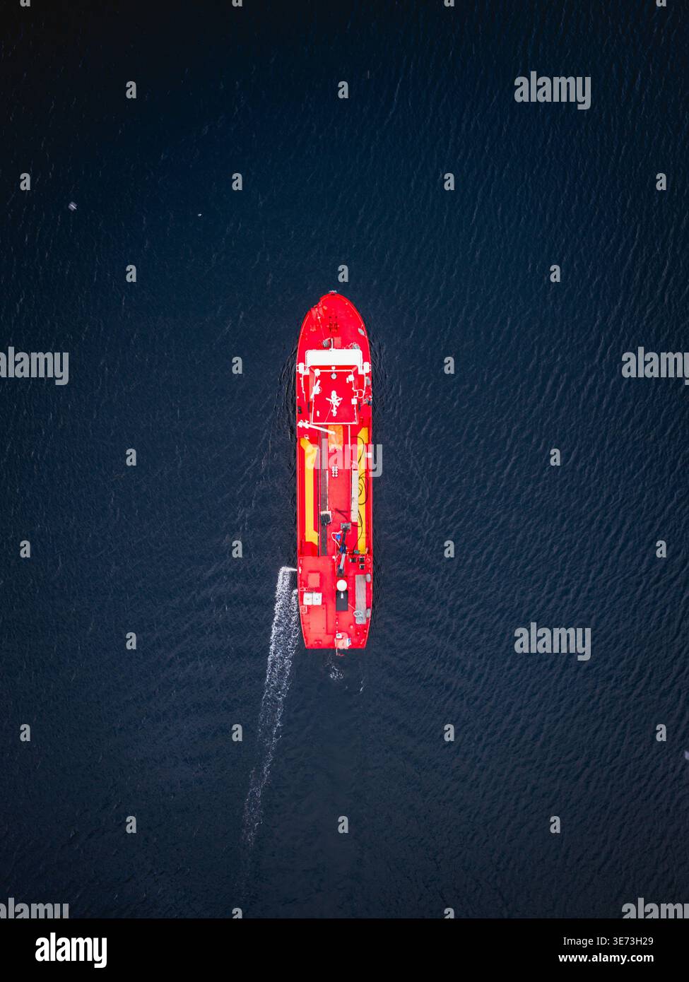 Veduta aerea di una vivace barca rossa che taglia le acque scure e strutturate al largo della costa, Ballstad, Nordland, Norvegia. Foto Stock