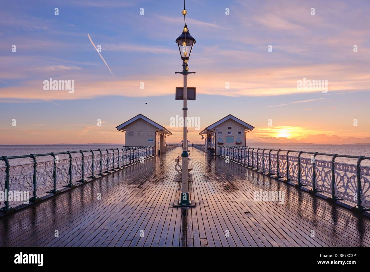 Penarth, Regno Unito - 16 gennaio 2026. Una vista simmetrica sul bagnato Penarth Pier che si affaccia all'alba, ringhiere di ferro ornate, un lampo vittoriano centrale Foto Stock