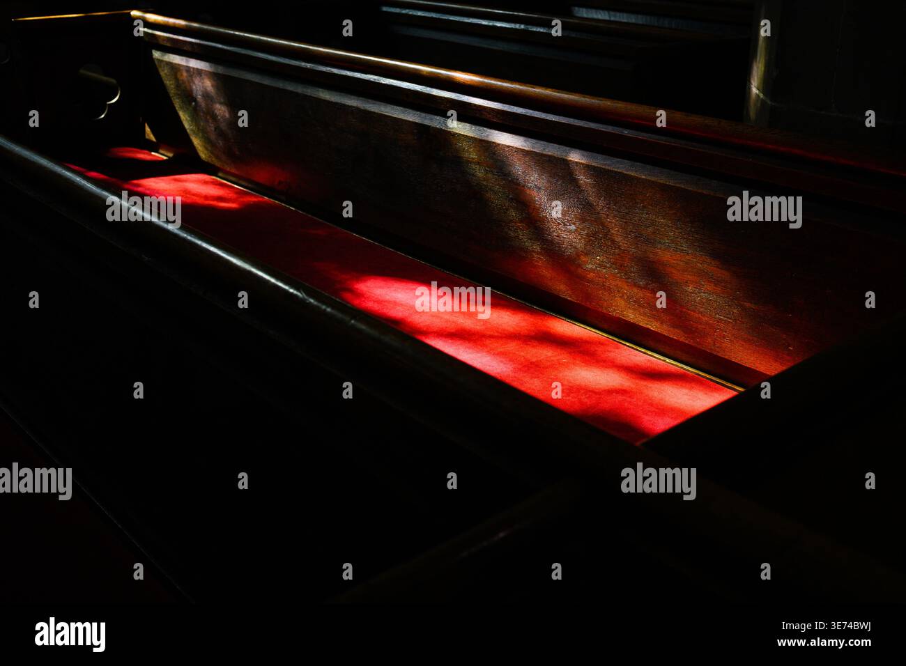 La luce del sole cade sul sedile rosso e sullo schienale in legno della vecchia chiesa con ombre nei dintorni Foto Stock