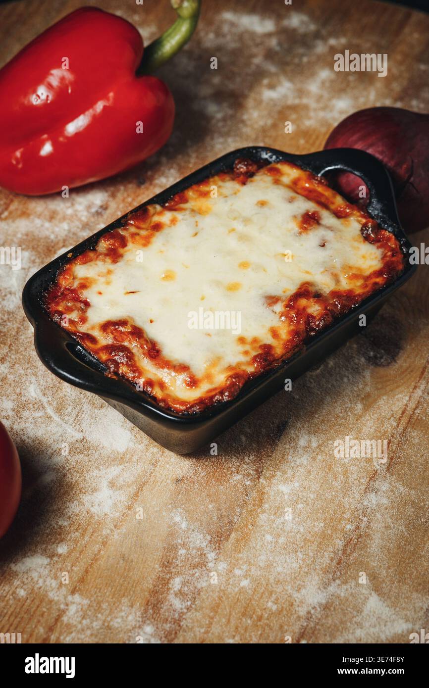 Lasagne di manzo tradizionali italiane con mozzarella fusa in un piatto da forno in ceramica nera su un tavolo rustico in legno infarinato. Foto Stock