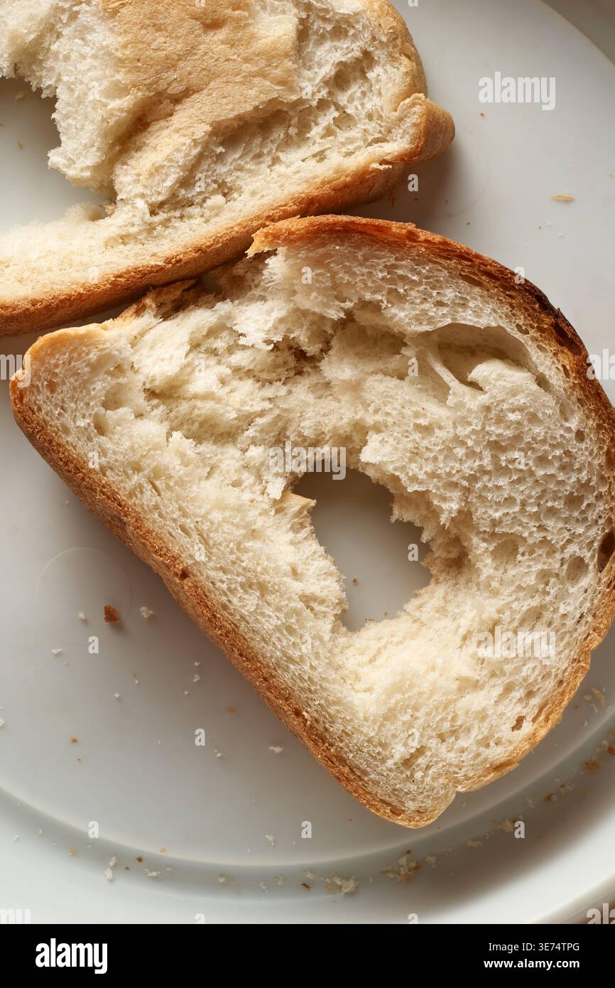pane bianco strappato con foro sul piatto, struttura porosa delle briciole e crosta tostata, vista dall'alto, concetto di povertà o semplice pasto quotidiano Foto Stock