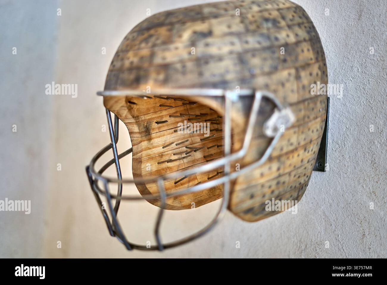 Una vista laterale ravvicinata di una scultura di casco da football americano in stile vintage montata su un muro di colore chiaro. Il casco è realizzato in legno con Foto Stock