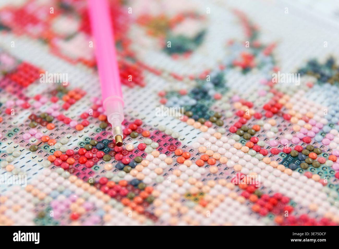 Primo piano di un colorato dipinto di diamanti in corso. Un applicatore rosa viene utilizzato per posizionare gemme scintillanti su un design floreale Foto Stock