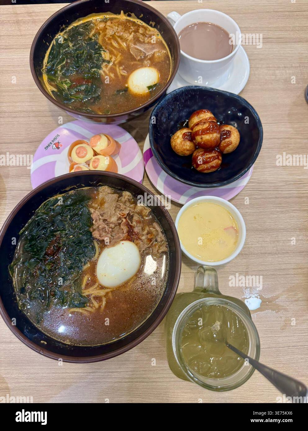 Piatto di un pasto giapponese al ristorante Miyagi: Due ciotole di ramen di manzo con alghe e uova, takoyaki, sushi di salmone e tè verde freddo. Foto Stock