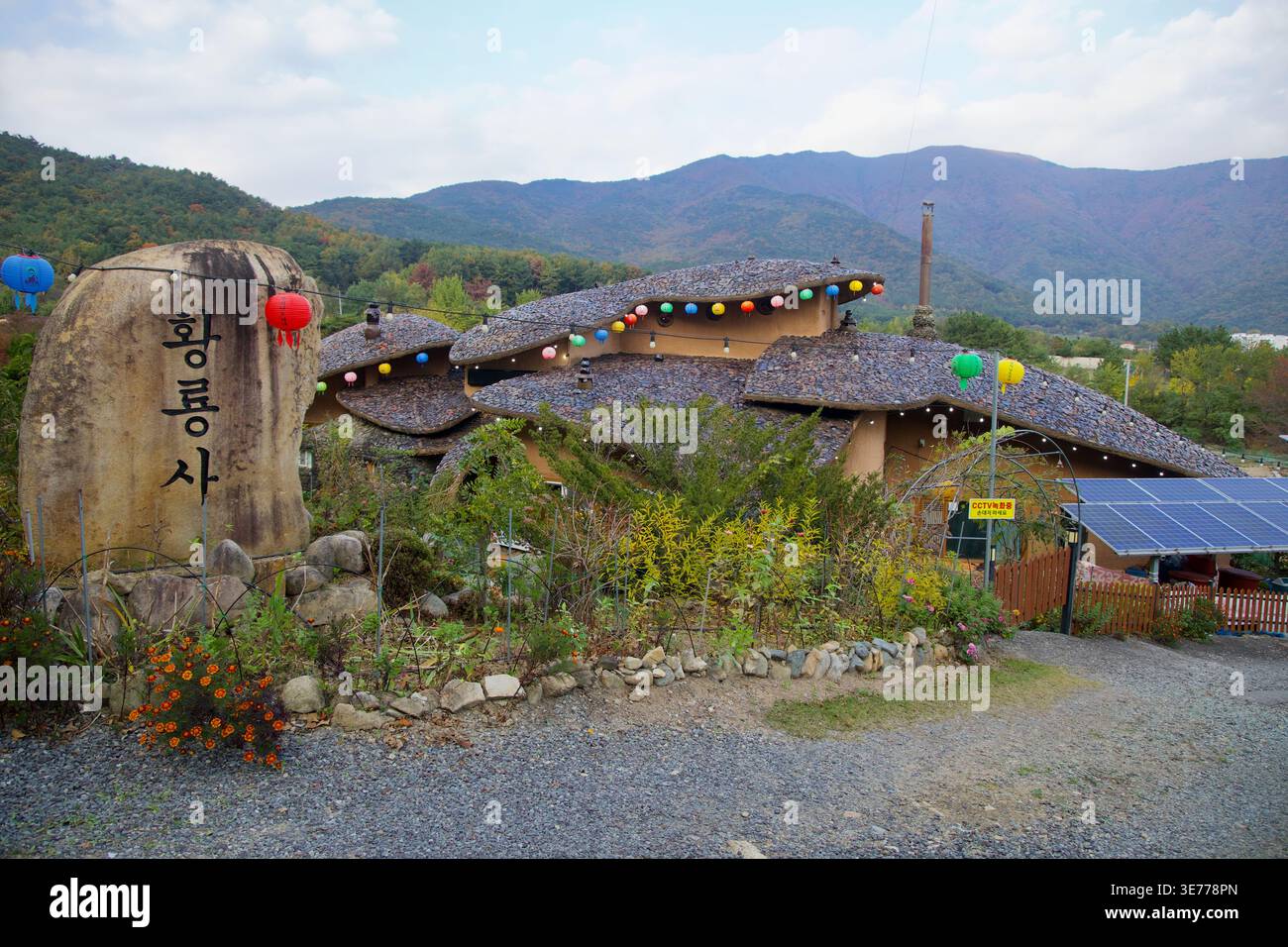 A Ulju-gun, Ulsan, un edificio stravagante con tetto curvo con lanterne, pannelli solari e piantagioni di giardini si trova sotto ampie creste di montagna in morbida foschia. Foto Stock