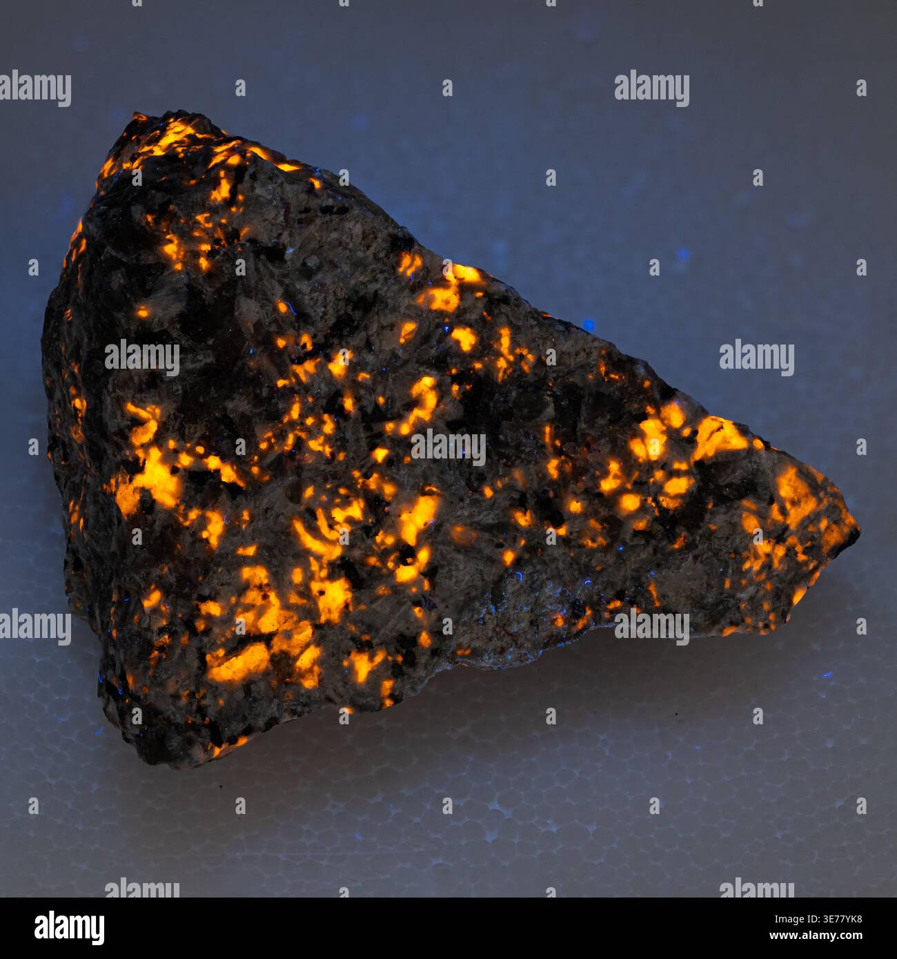 Primo piano di un campione minerale fluorescente che emette una calda luce dorata per la scienza e la geologia Foto Stock