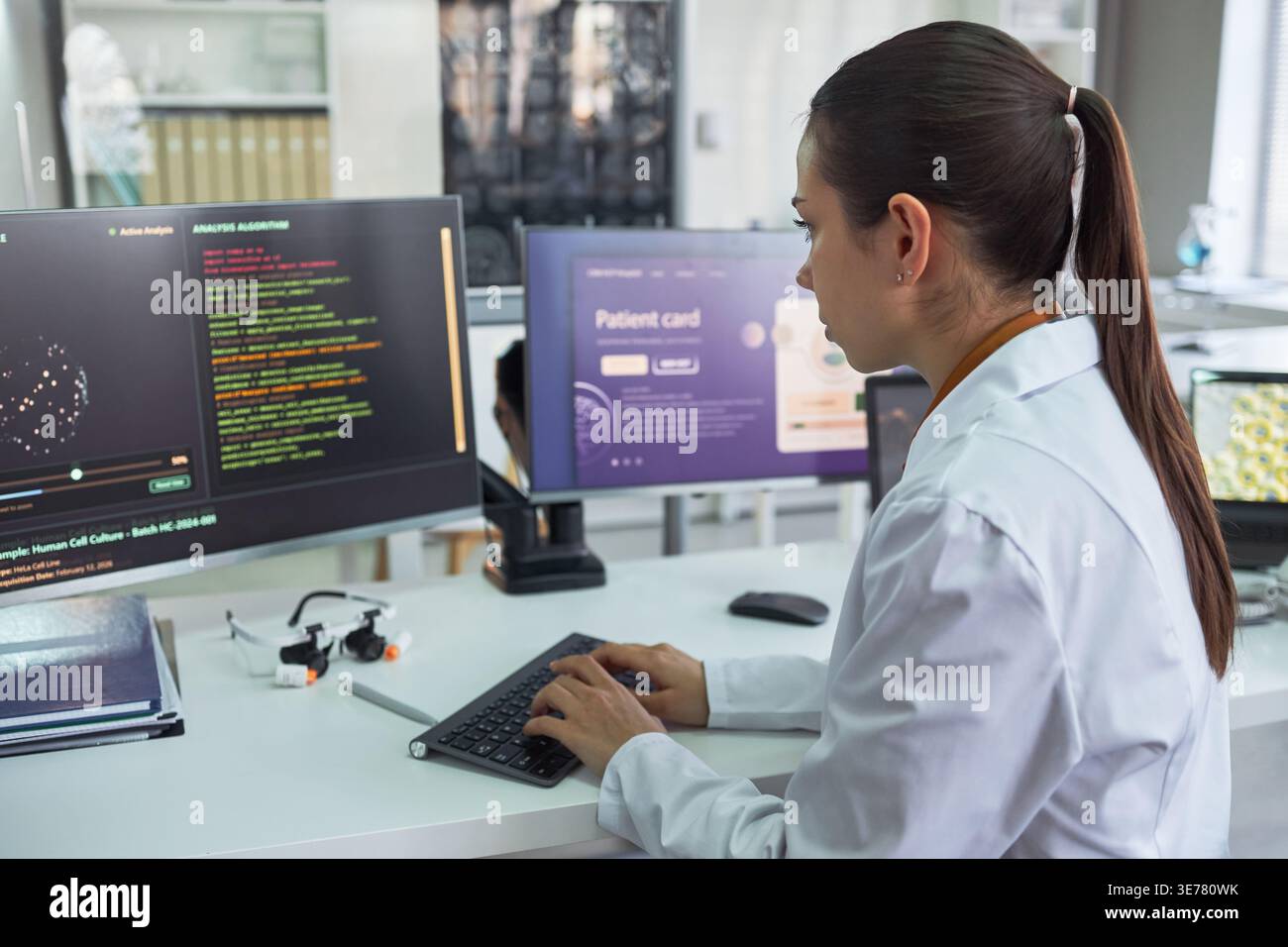 Giovane donna caucasica adulta che analizza i dati medici su monitor desktop, digitando nello spazio di lavoro del laboratorio. Ideale per tecnologie sanitarie, software di diagnostica e marketing di ricerca Foto Stock