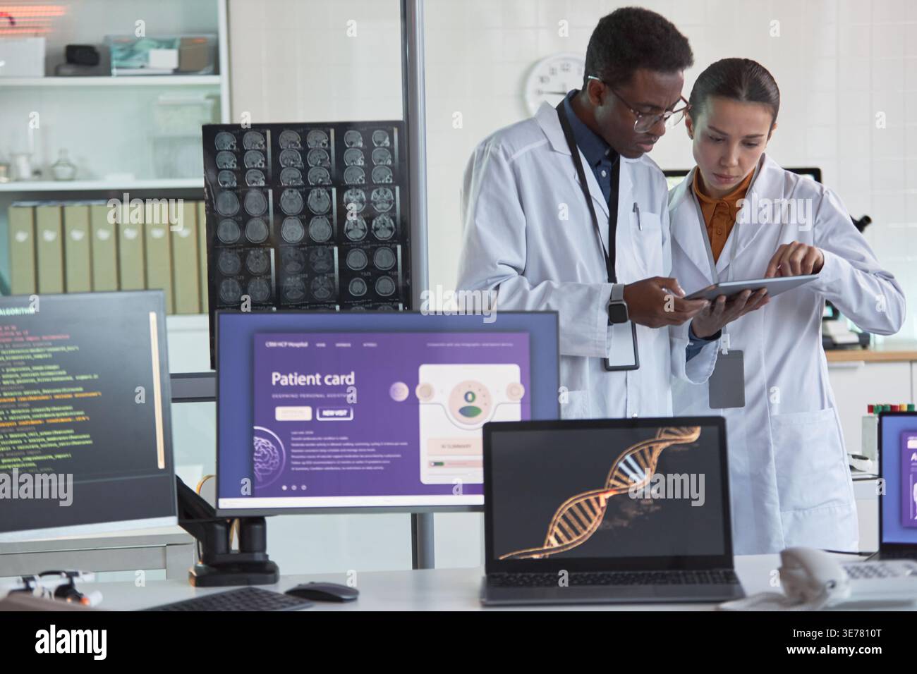 Medico afroamericano maschile e scienziata asiatica donna che esamina tablet in laboratorio medico, analizzando i dati dei pazienti e la ricerca. Ideale per la tecnologia sanitaria, la diagnostica e il marketing del lavoro di squadra Foto Stock