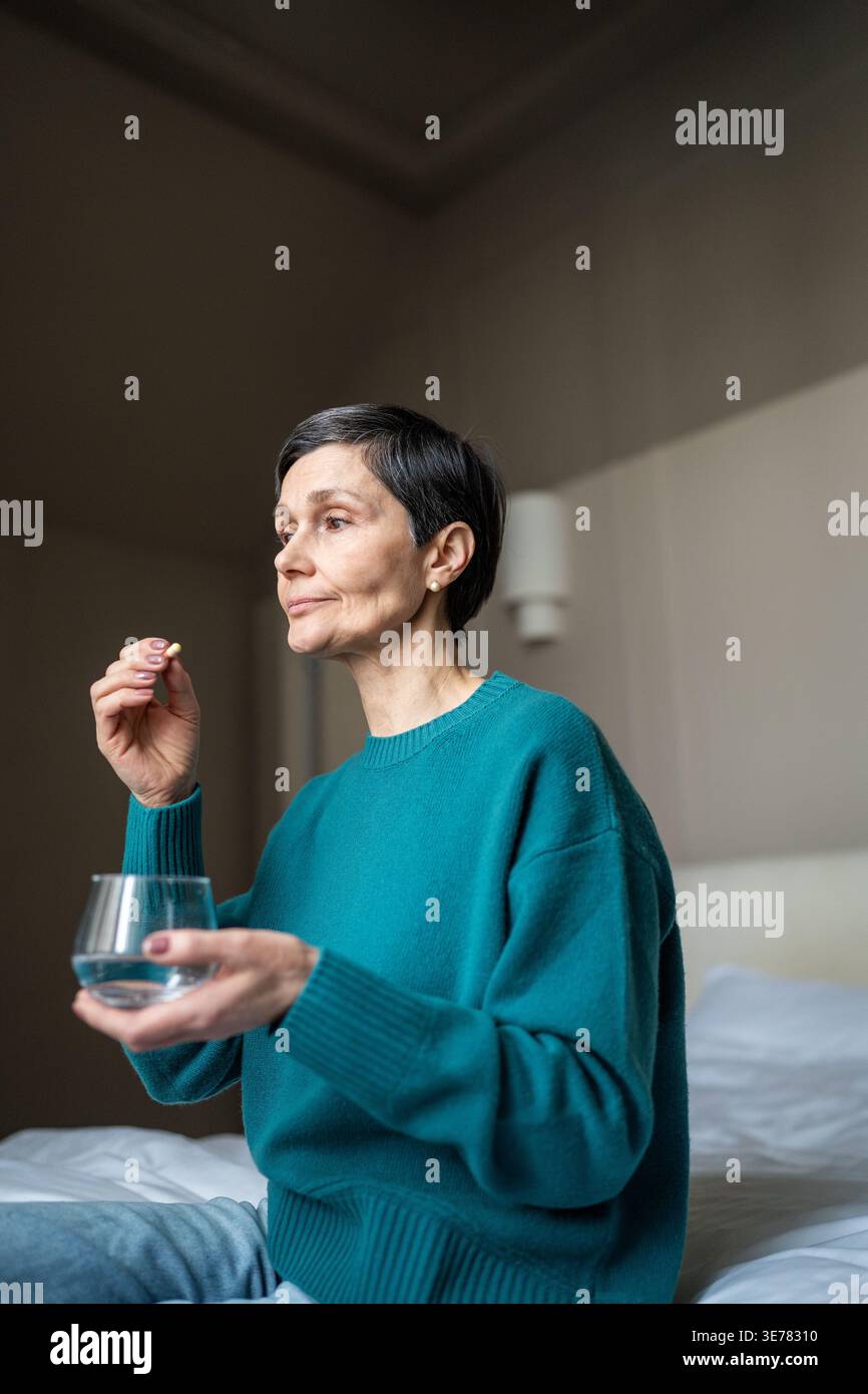 Donna anziana che prende medicine speciali per curare la malattia, tenendo un bicchiere d'acqua e un integratore di pillole. Foto Stock