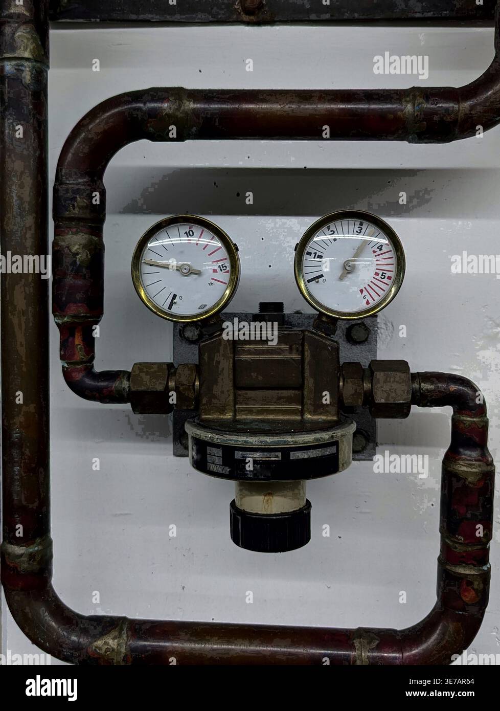 Vista dettagliata di due manometri analogici montati su un regolatore in ottone, collegati a un sistema di tubi in rame invecchiato contro una parete bianca semplice, Showi Foto Stock