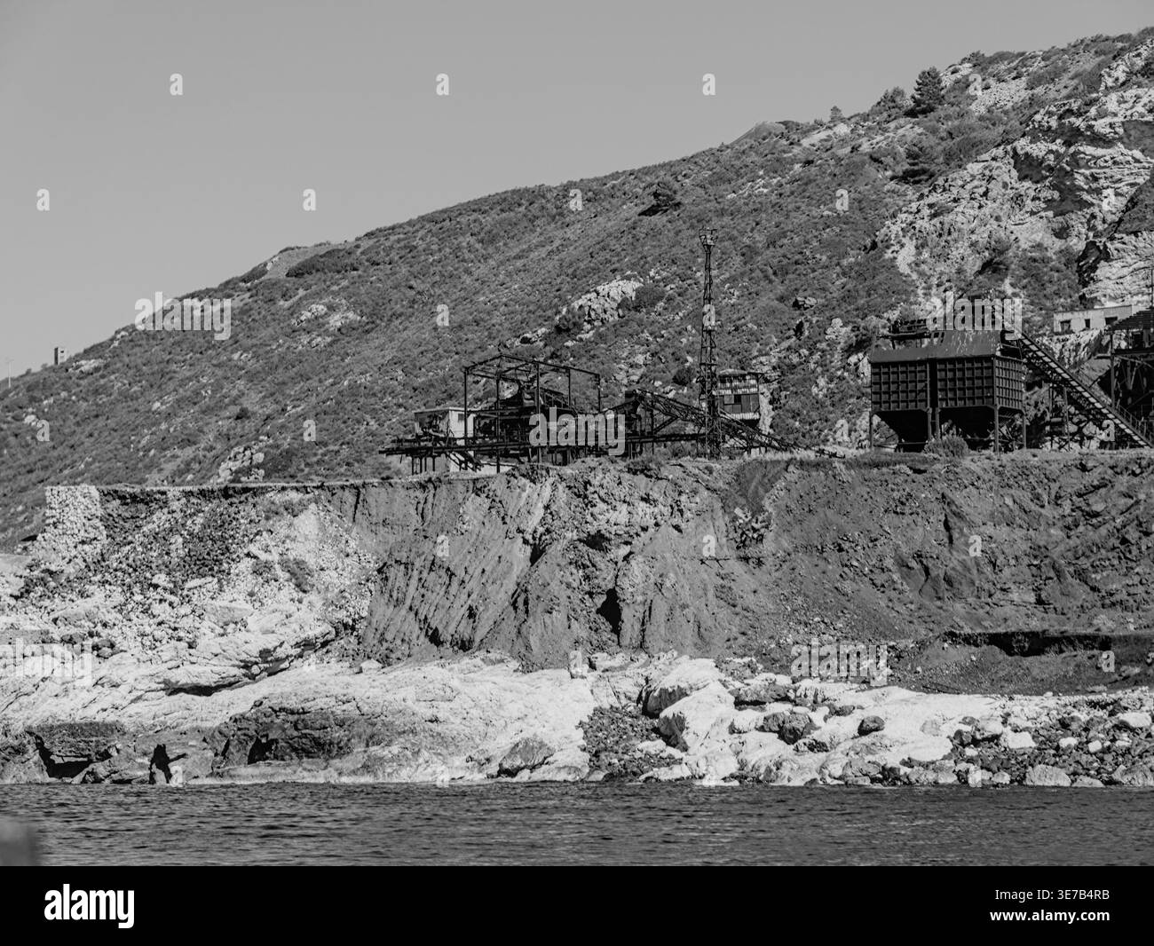 Una dettagliata vista monocromatica della principale struttura industriale che si affaccia sul mare sulla costa frastagliata dell'Elba. Foto Stock
