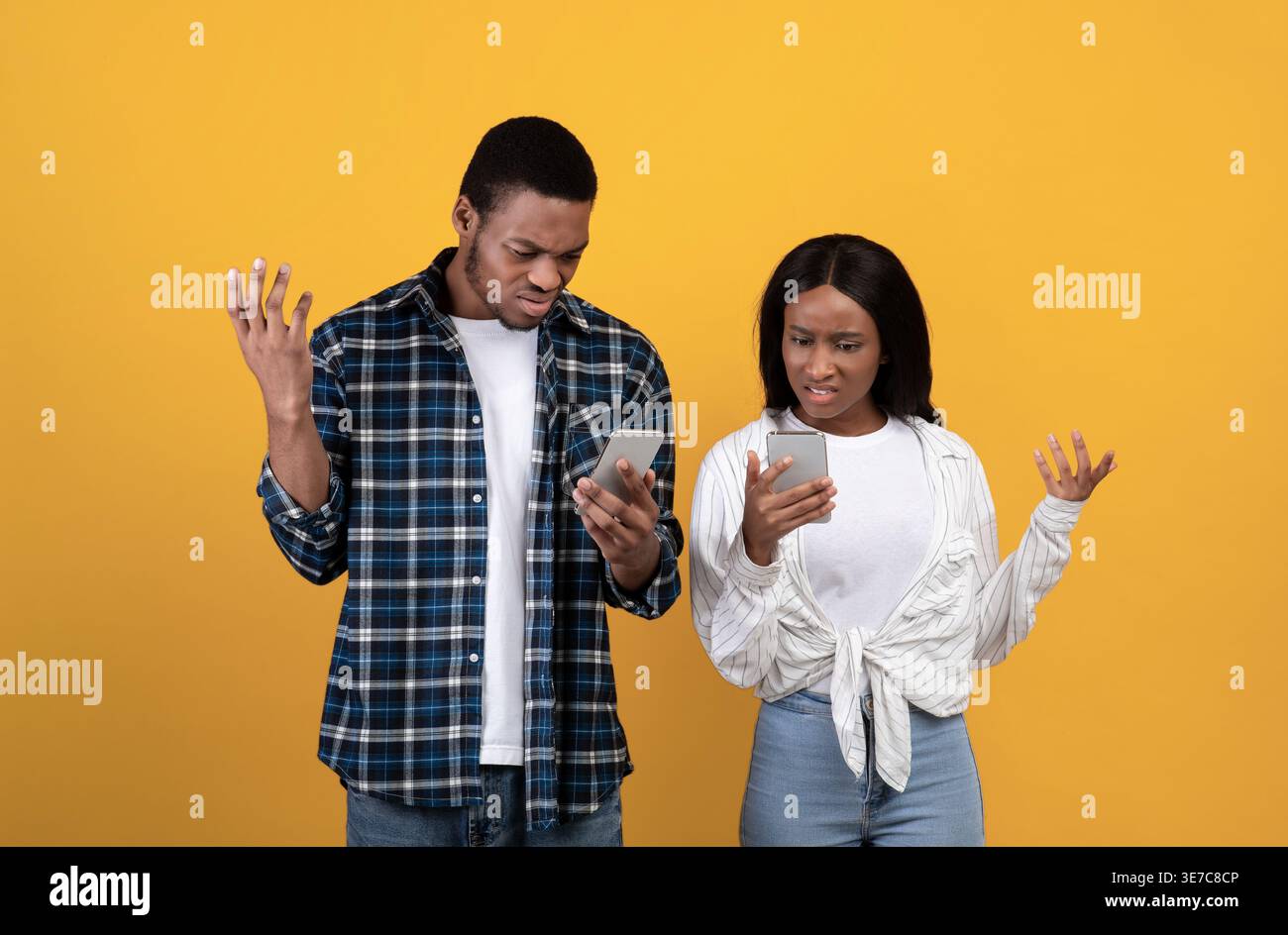 Coppia nera che utilizza gli smartphone mentre si trova sullo sfondo giallo in studio Foto Stock
