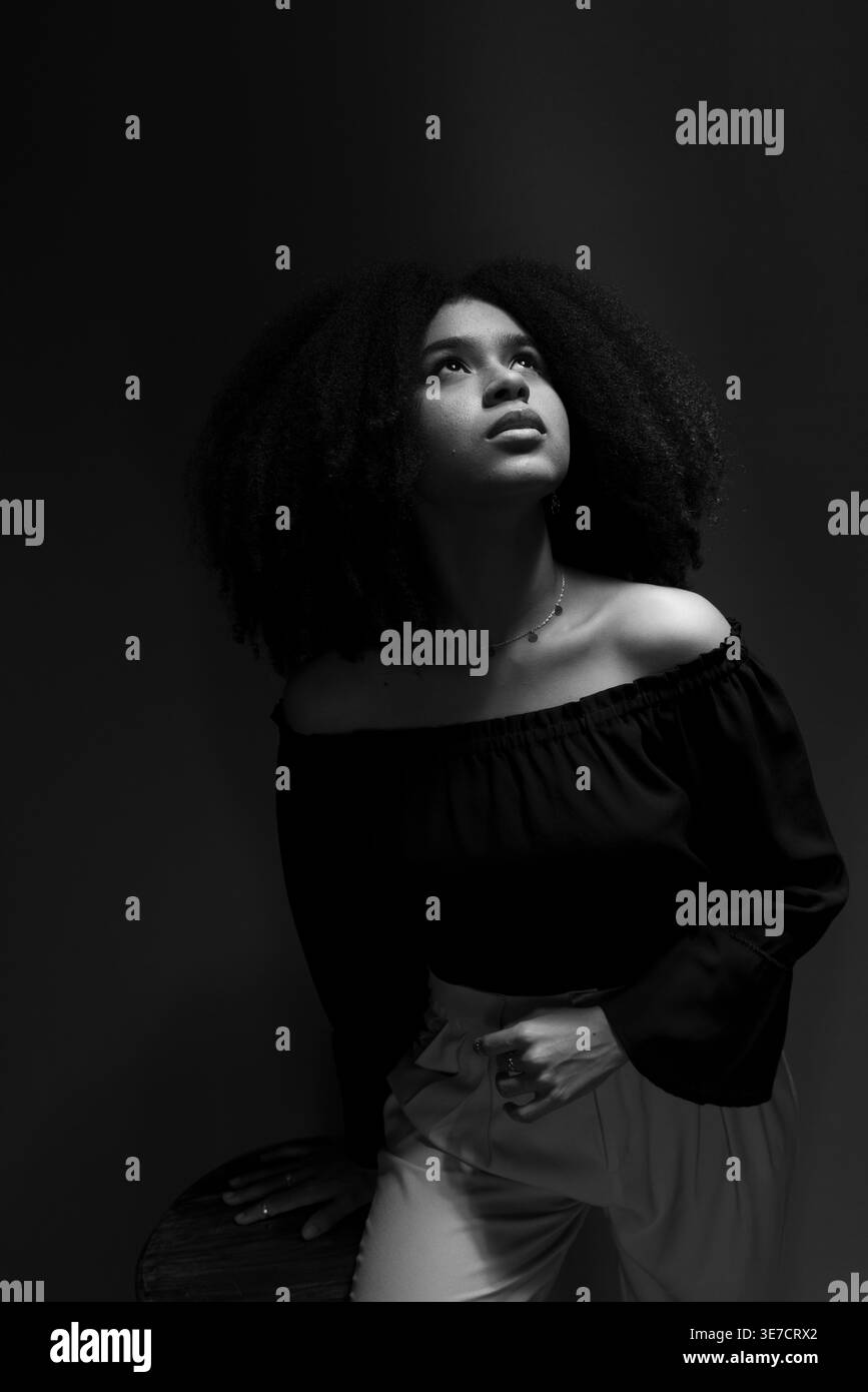 Donna nera con afro riccio che guarda in alto mentre si trova in uno studio oscuro Foto Stock