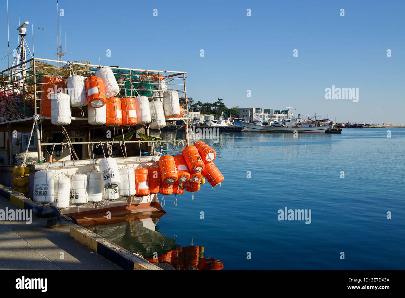 Al porto di Bangeojin a Ulsan, boe arancioni e bianche pendono da uno scaffale sopra l'acqua del porto con barche in servizio attraverso il bacino. Foto Stock
