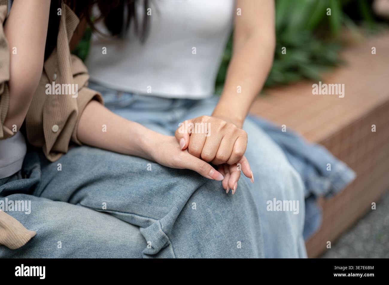 Donna asiatica che tiene la mano del suo amico mentre siede insieme sulla panchina in giardino Foto Stock