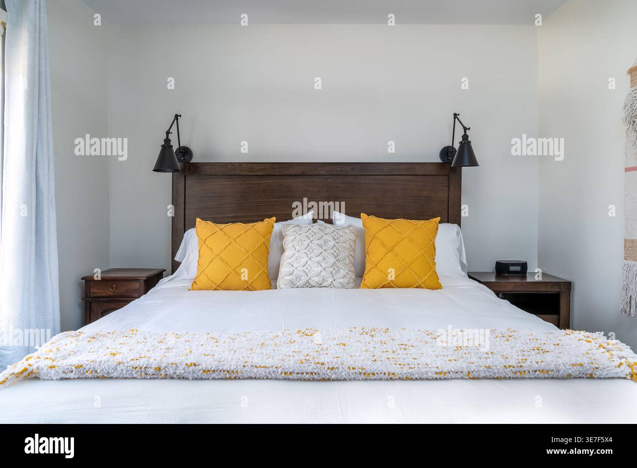 Moderna camera da letto bianca in agriturismo con letto, testiera, cuscini gialli decorativi, lampade nere Foto Stock