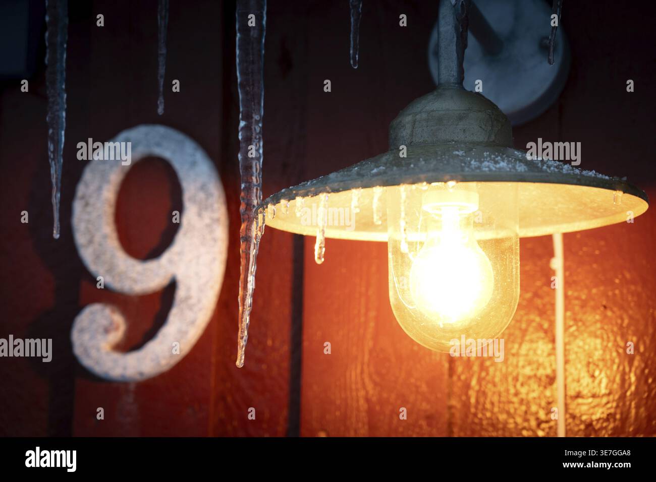 Una lampada con ghiaccioli è appesa accanto a un numero di metallo 9, illuminata al buio, una lampada illuminata con ghiaccioli è appesa al buio accanto a una casa numero 9 Foto Stock
