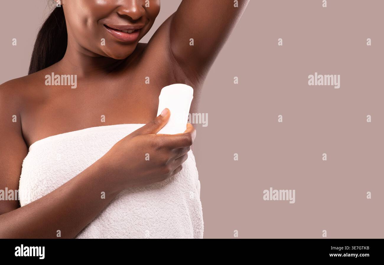 Donna nera avvolta in un asciugamano con deodorante mentre si trova su uno sfondo marrone rosato in studio Foto Stock