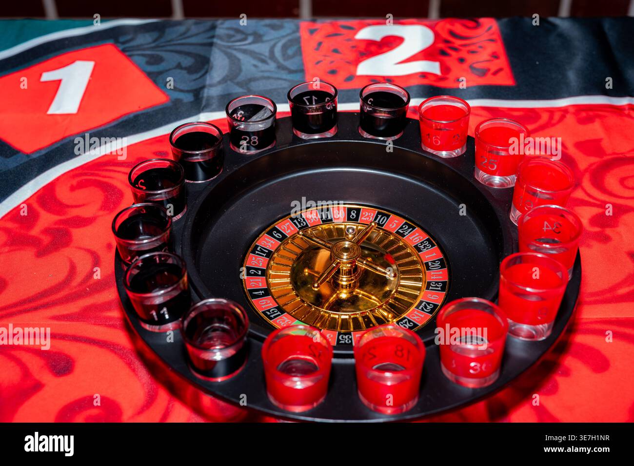 Sparare bicchieri pieni di liquidi rossi e neri che circondano una roulette in miniatura su un tappetino da gioco a tema, creando la scena per una festa o giù di lì Foto Stock