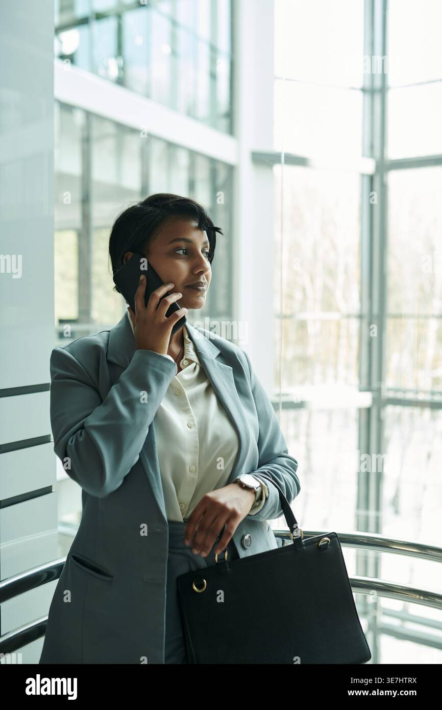 Donna d'affari mista che riceve telefonate mentre si trova in ascensore durante il giorno Foto Stock
