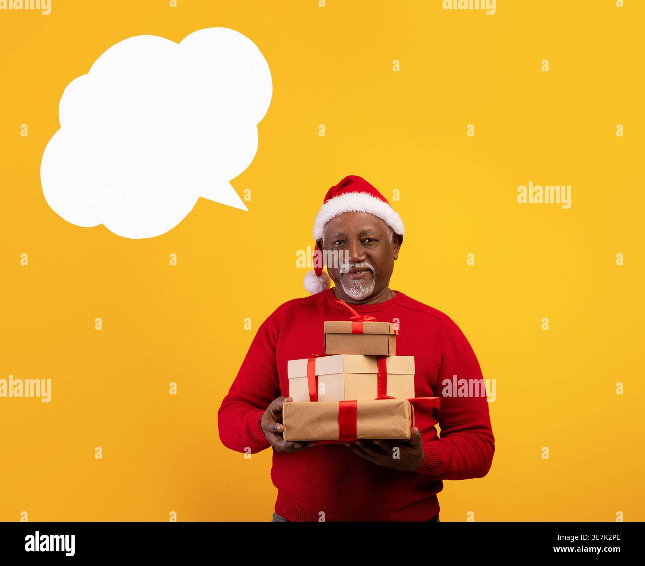 Uomo nero di mezza età che indossa il cappello di Babbo Natale e regge scatole regalo su sfondo giallo con una bolla vuota in studio Foto Stock