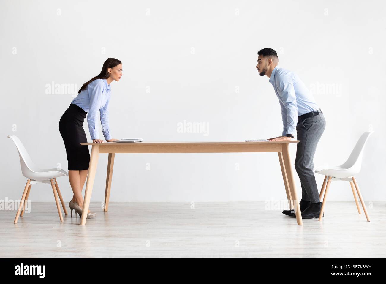 Uomo e collega mediorientale in piedi uno di fronte all'altro alla lunga scrivania in ufficio Foto Stock