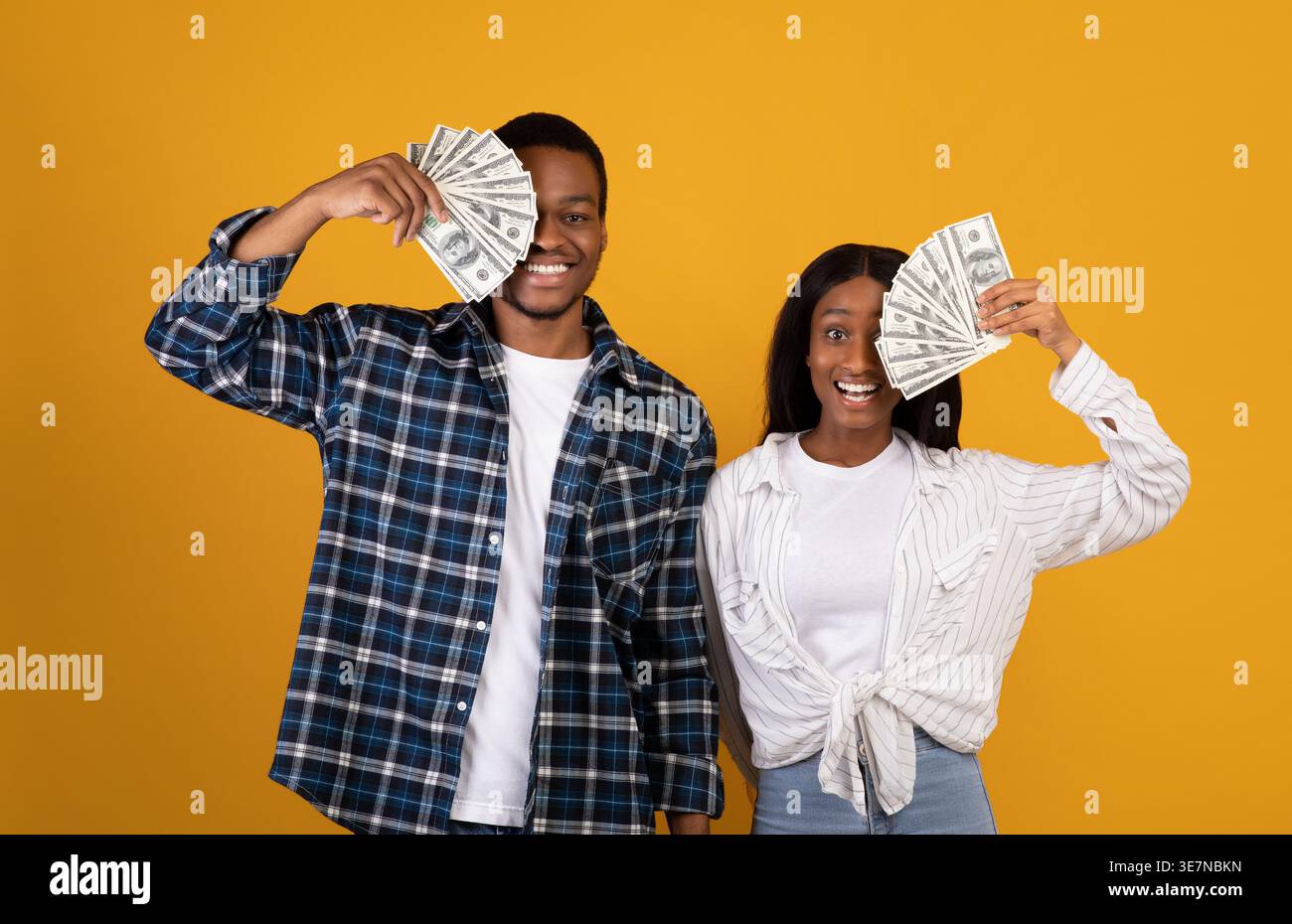 Coppia nera che copre gli occhi con i money mentre si trova su sfondo giallo in studio Foto Stock