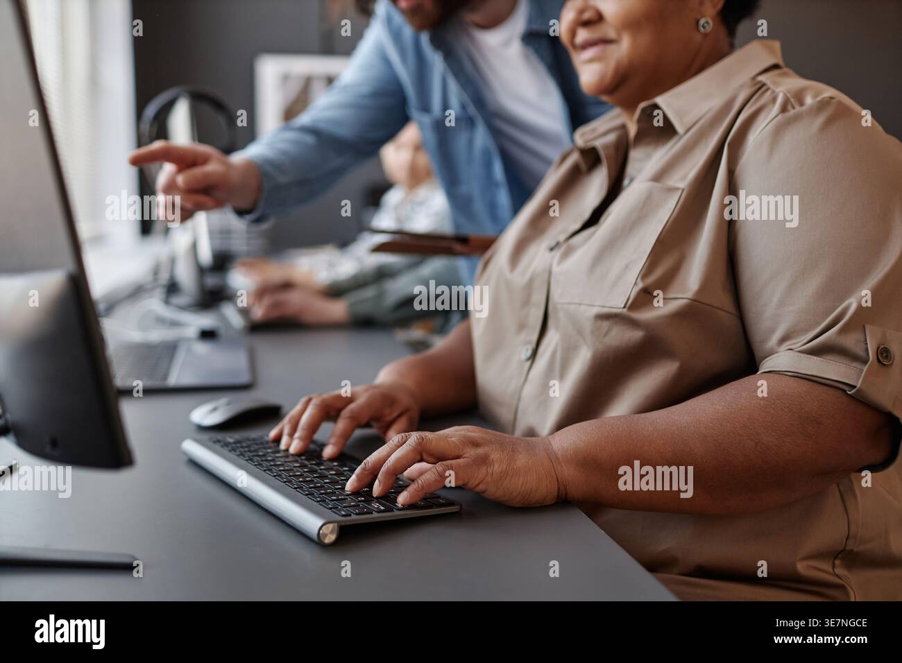 Immagine ritagliata di una donna nera di mezza età che digita sulla tastiera mentre ascolta un insegnante DI INFORMATICA durante la lezione in sala computer Foto Stock