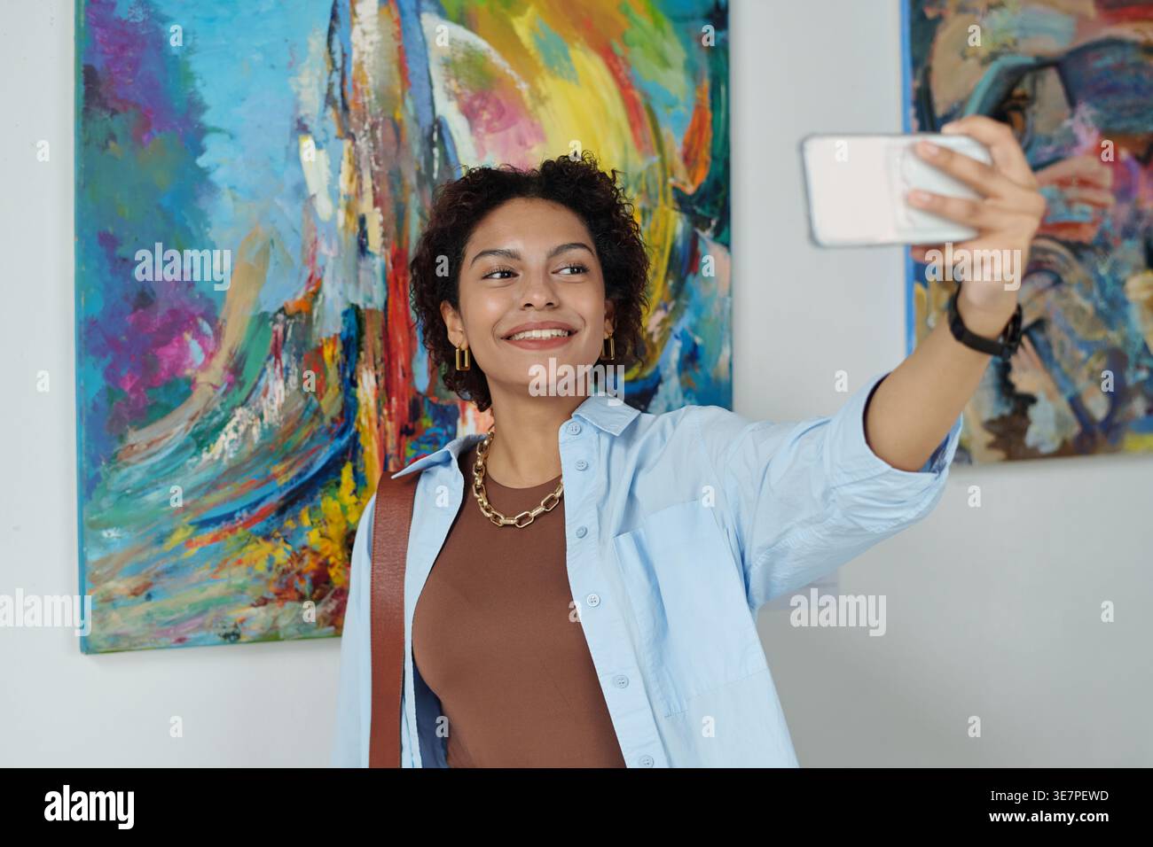 Adolescente nera che scatta selfie contro i dipinti mentre è in piedi nella galleria d'arte Foto Stock