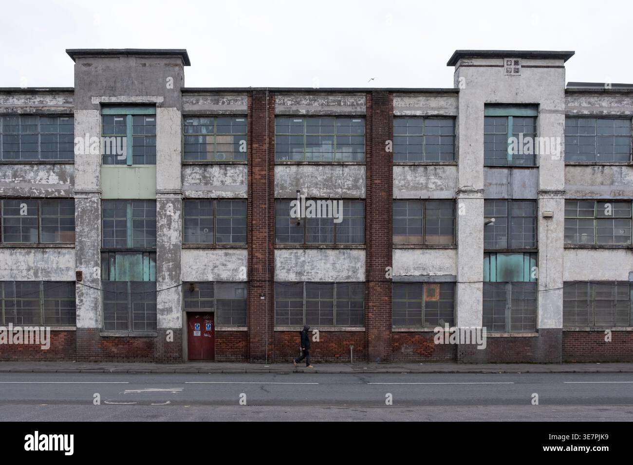 Facciata frontale simmetrica della Carlton Die Castings Ltd, un edificio di magazzino in rovina precedentemente una fabbrica di tabacco, con un passante, Paisley, Scozia. Foto Stock