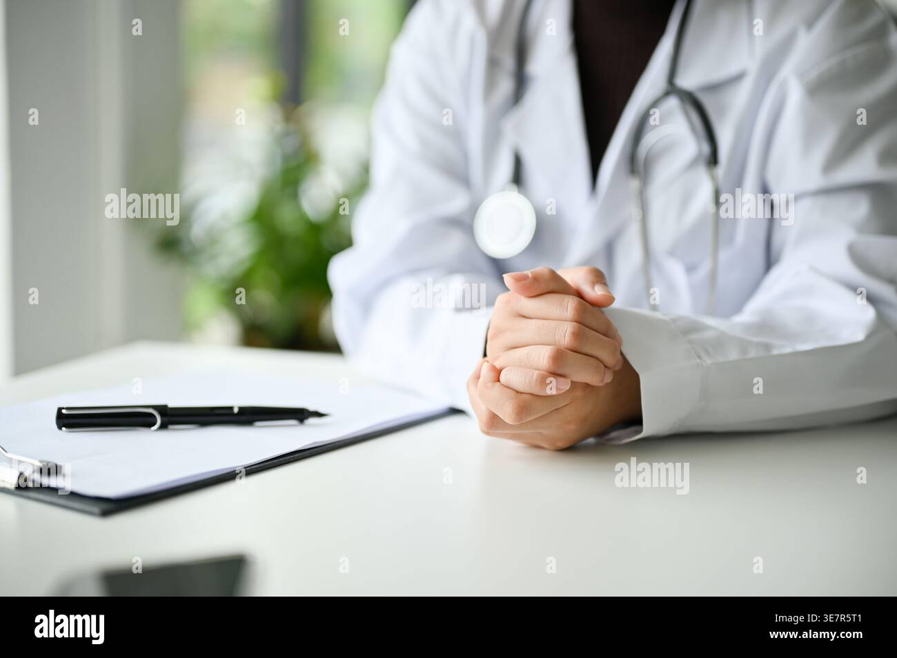 Donna asiatica dottore seduto con le mani schiacciate a tavola in clinica Foto Stock