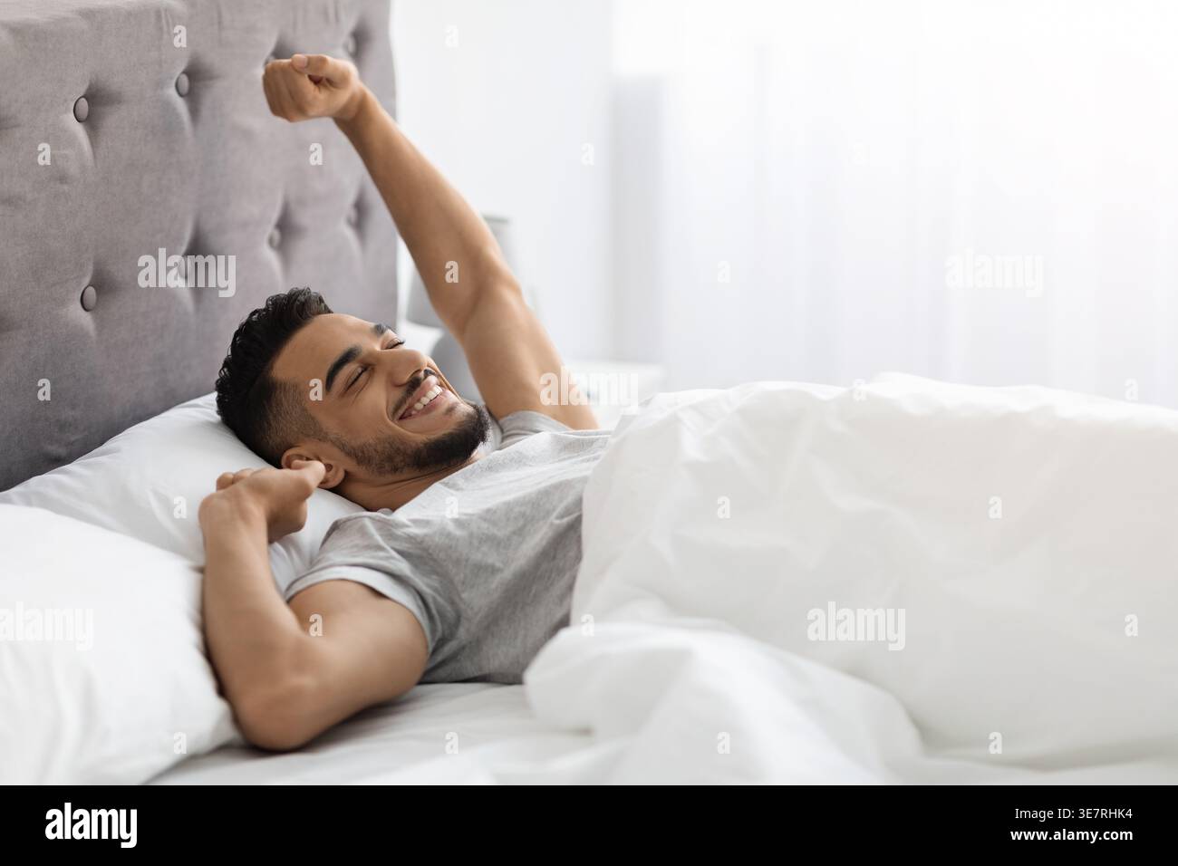 Uomo arabo che allunga le braccia mentre sdraiato sul letto nella camera da letto di casa Foto Stock