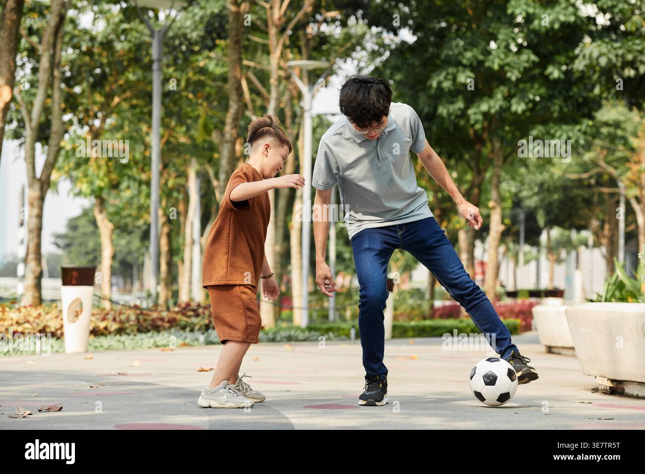 Padre asiatico che gioca a calcio con il figlio nel parco Foto Stock