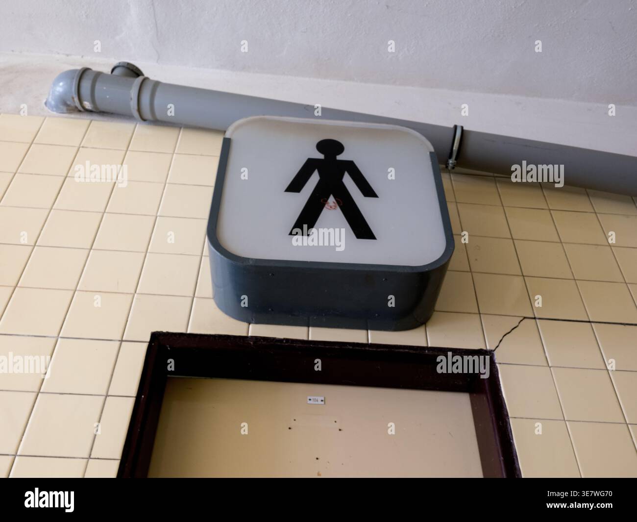 Insegna di toilette maschile retrò illuminata con un bastoncino nero su una parete piastrellata all'interno di un edificio pubblico nella Repubblica Ceca Foto Stock
