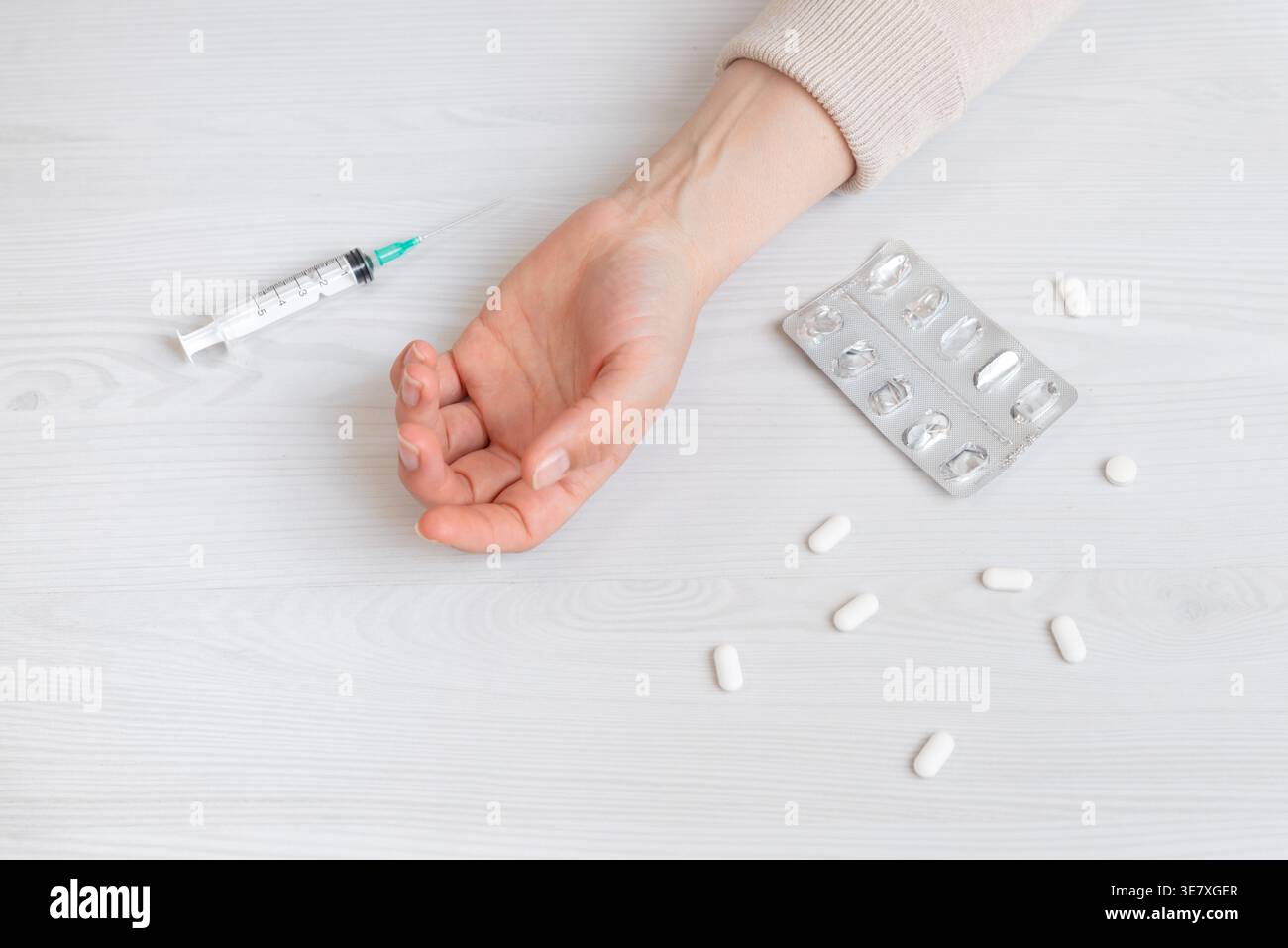 Mano appoggiata accanto a pillole e siringa, concetto di sovradosaggio, dipendenza e emergenza medica Foto Stock