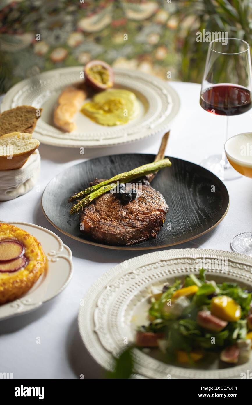 Cena a base di bistecche con asparagi e vino in tavola Foto Stock