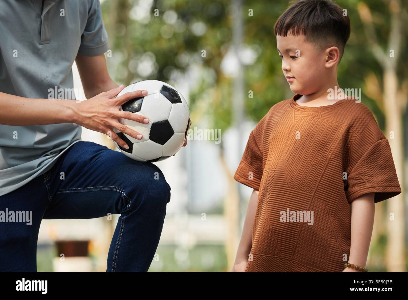 Ragazzo asiatico che impara il calcio con il padre nel parco Foto Stock