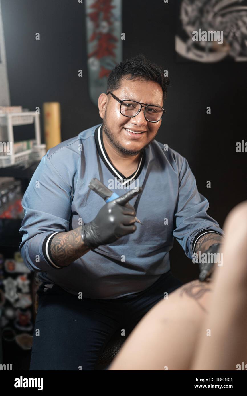 Artista di tatuaggio ispanico maschile che indossa guanti in nitrile nero tenendo in mano la macchina per tatuaggi mentre lavora nel suo studio Foto Stock