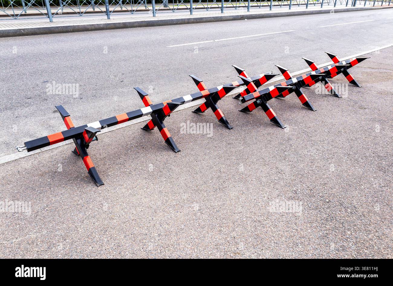 Barriera stradale in metallo con motivo di attenzione a strisce rosse, nere e bianche, recinzione stradale sulla strada della città. Barriere stradali di sicurezza in città Foto Stock