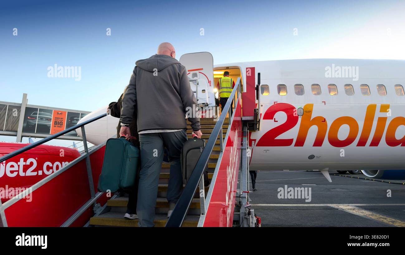 I passeggeri che salgono su un aereo commerciale Jet2holidays tramite scale portatili presso un terminal dell'aeroporto sotto un cielo limpido - Immagine stock catturata con smartphone