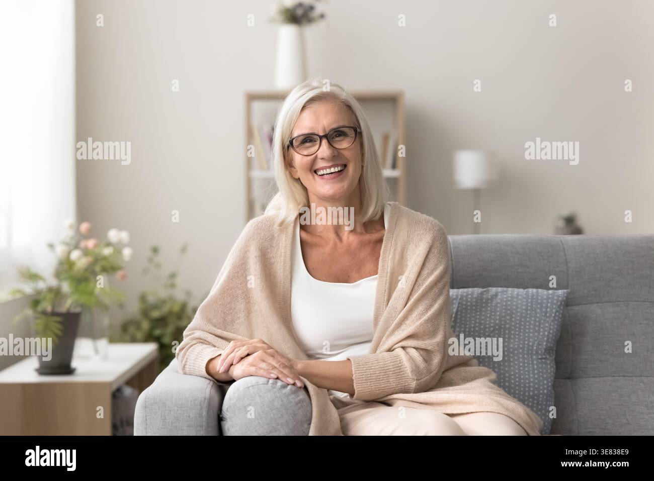 Nell'accogliente soggiorno una donna matura che posa seduta sul divano Foto Stock