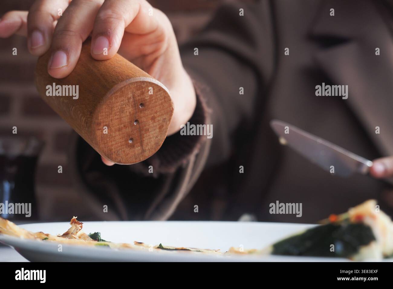 La persona aggiunge sale al cibo su un piatto bianco a un tavolo Foto Stock