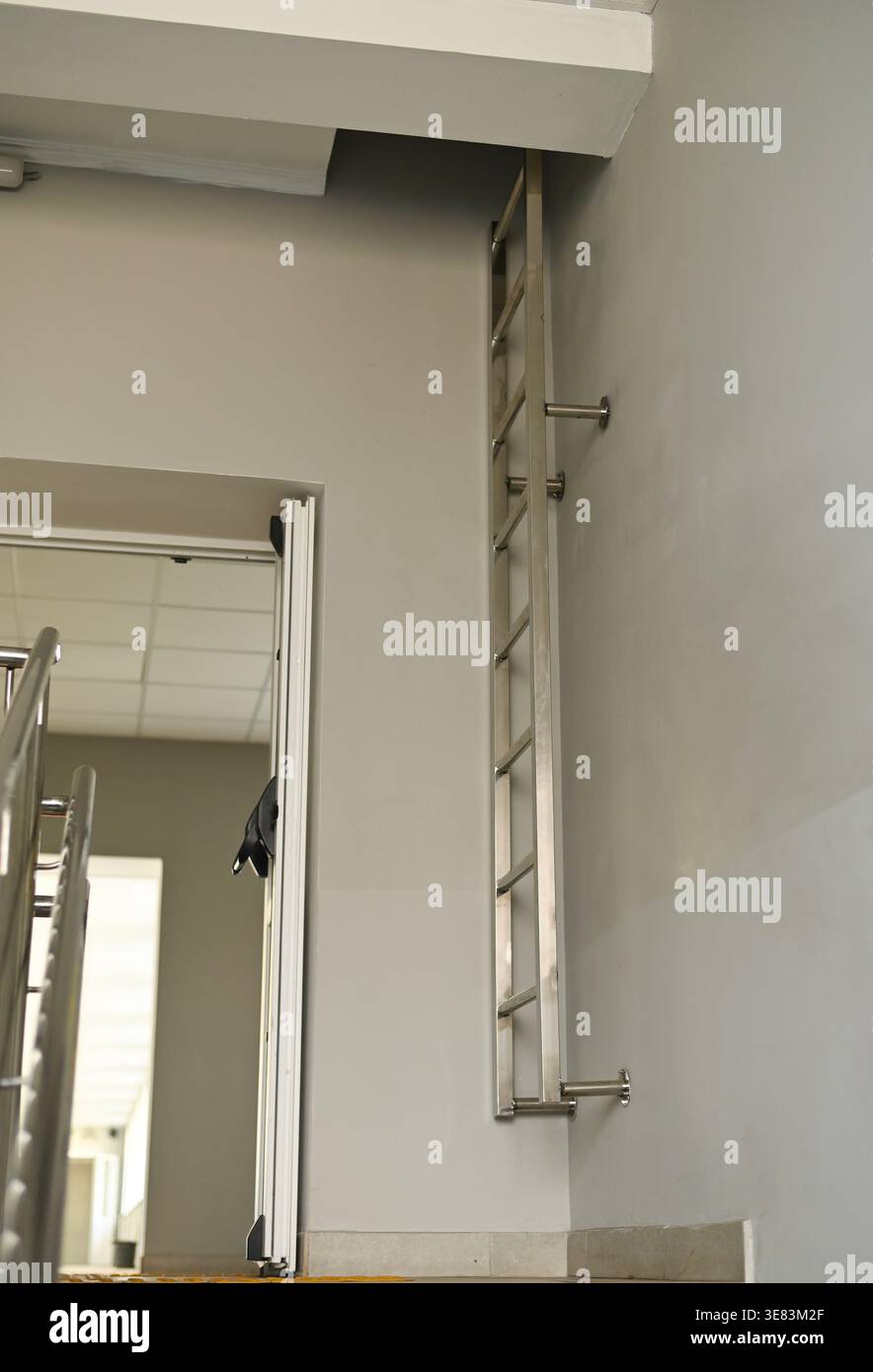 Scala tagliafuoco in metallo montata a parete all'interno dell'edificio, scala verticale stretta fissata alla parete, attrezzatura di sicurezza interna con cartelli numerati, funzionale e p Foto Stock