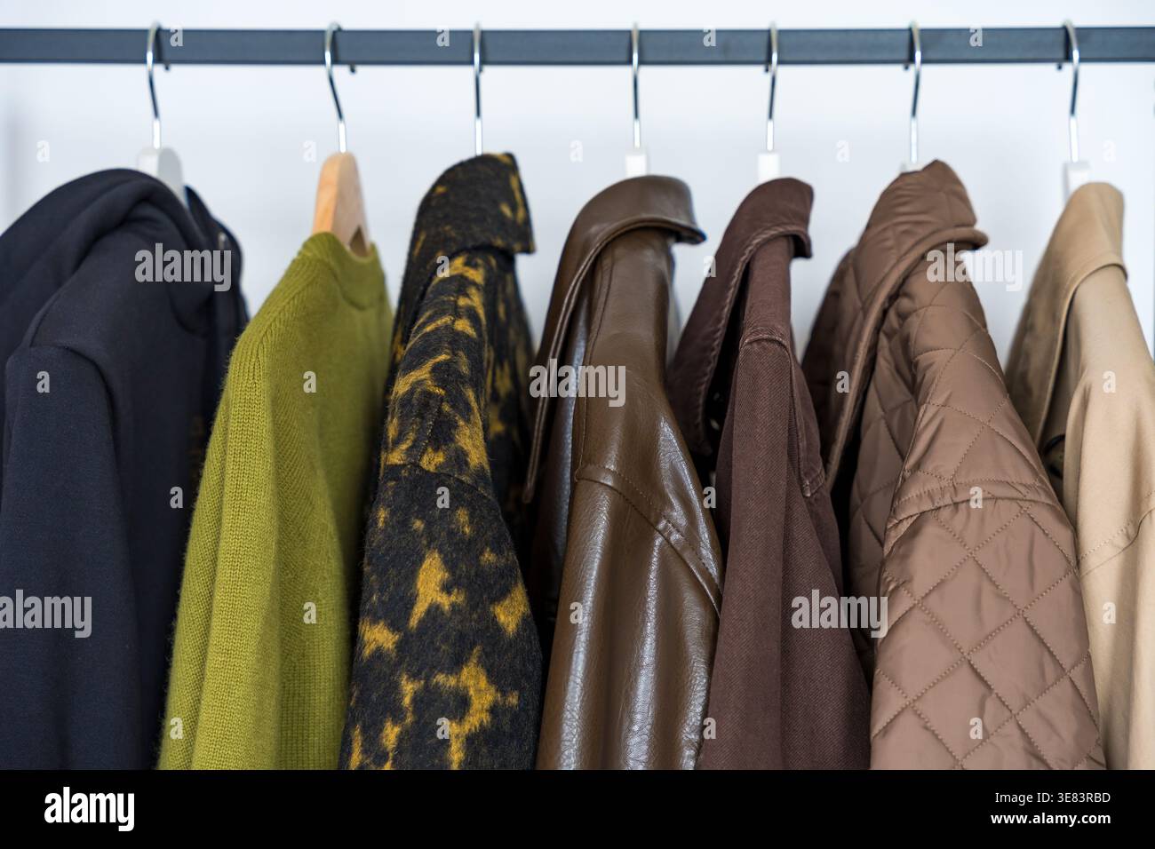 Una fila di cappotti autunnali, invernali e primaverili in tonalità terrose appesi su un elegante appendiabiti. Foto Stock