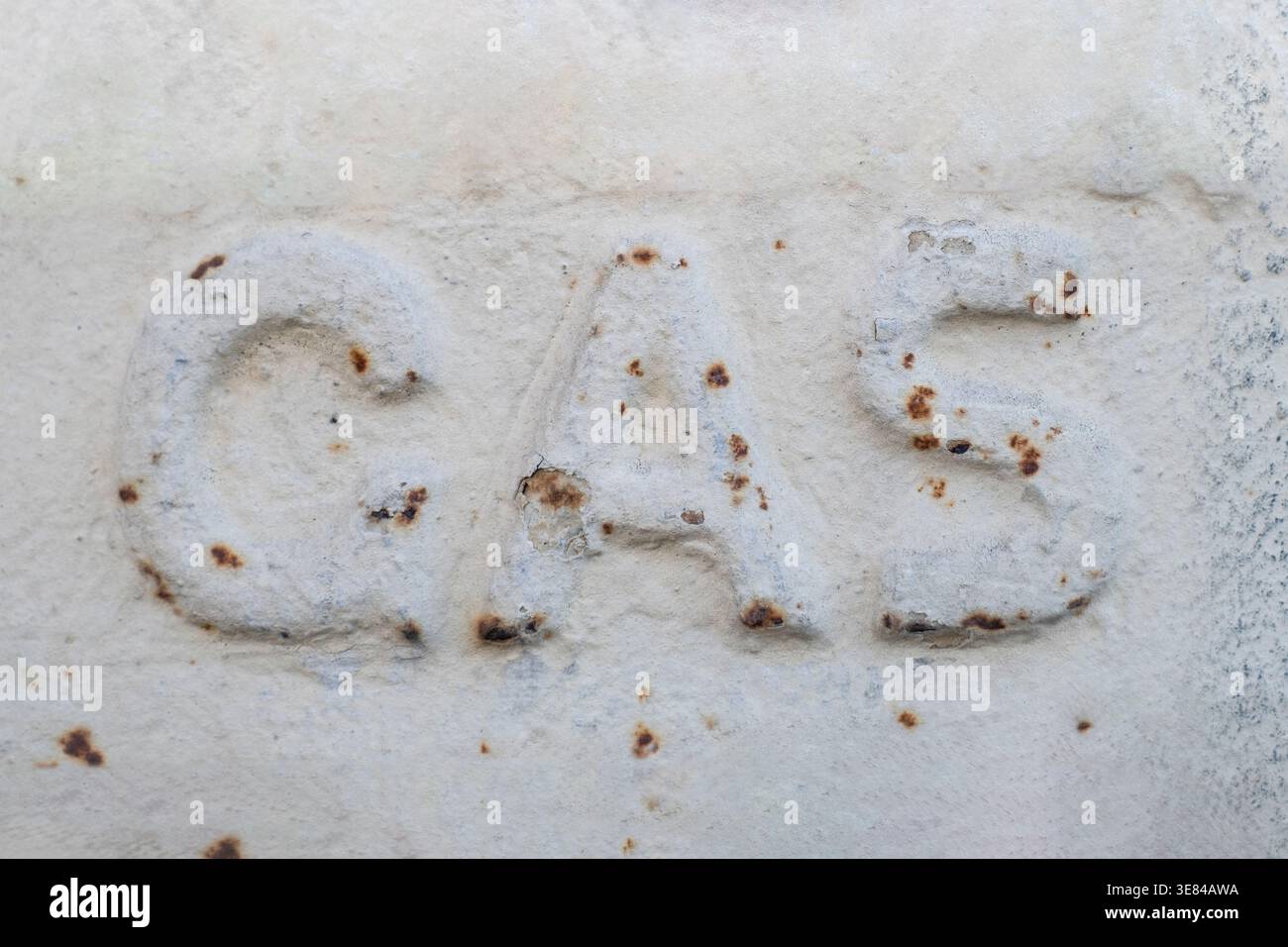 La parola GAS impressa su una piastra in ghisa in una strada urbana e dipinta con smalto bianco, sono visibili macchie di ruggine Foto Stock
