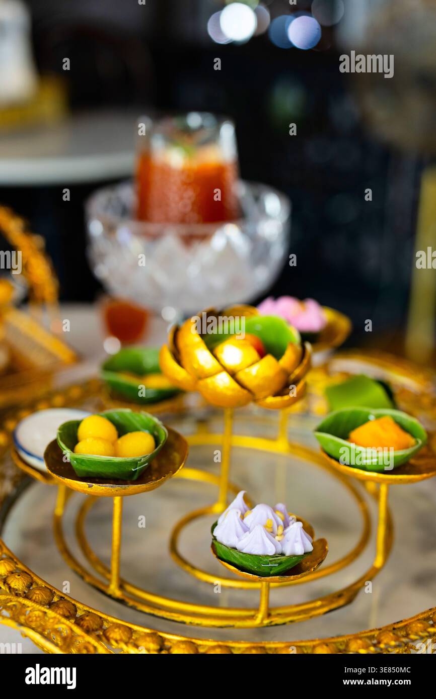 Tè pomeridiano di lusso su un tavolo in marmo con bancarelle dorate ornate che ospitano dessert assortiti e frutta, con tè freddo e bevande e bokeh Cafe bac Foto Stock