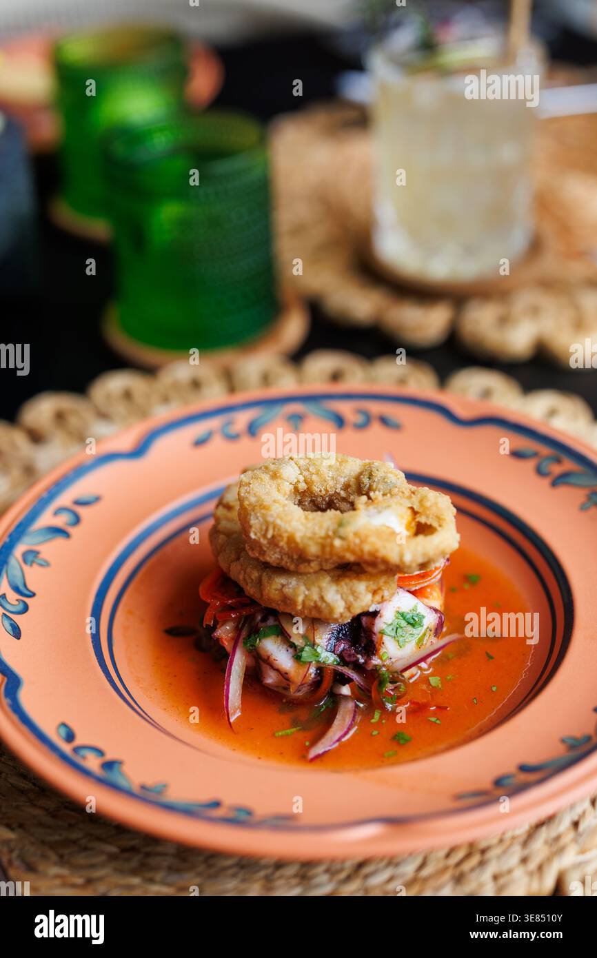 Antipasto gourmet di pesce fritto con cipolle tagliate ed erbe aromatiche in salsa di pomodoro su un piatto decorativo, bassa profondità di campo, intimi setti del ristorante Foto Stock