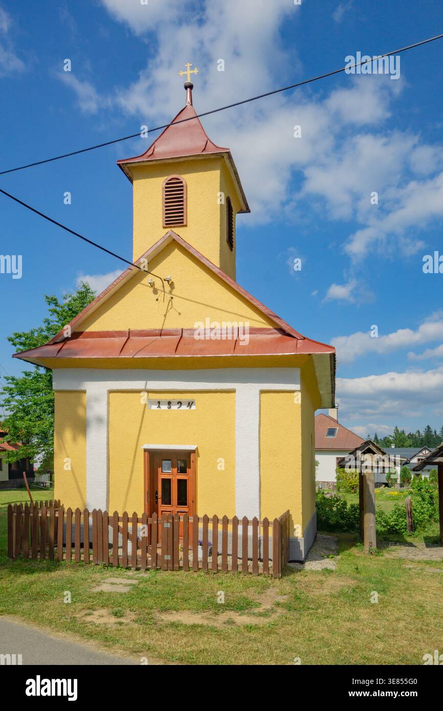 La vista di una piccola e vibrante cappella gialla con un tetto rosso si erge orgogliosamente sullo sfondo di un cielo blu con soffici nuvole, Donovaly, Banskobystricky k Foto Stock